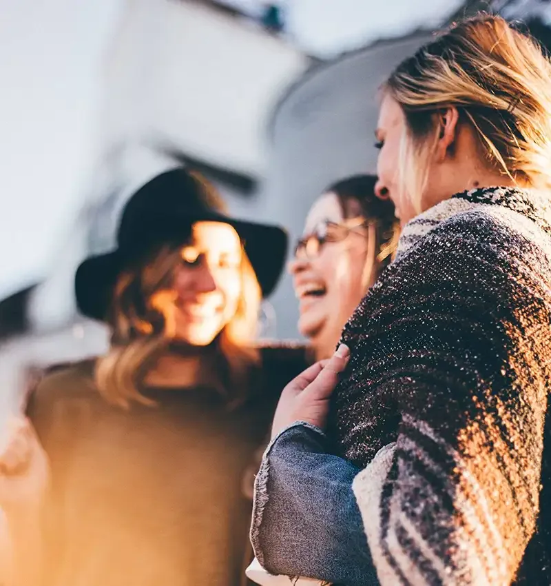 Three friends laughing together outdoors in warm late-afternoon light.